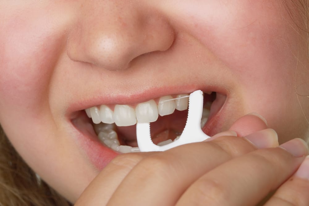 Dental Floss Types: Which Is Right For Your Teeth? 3 Young girl using a floss pick to clean her teeth