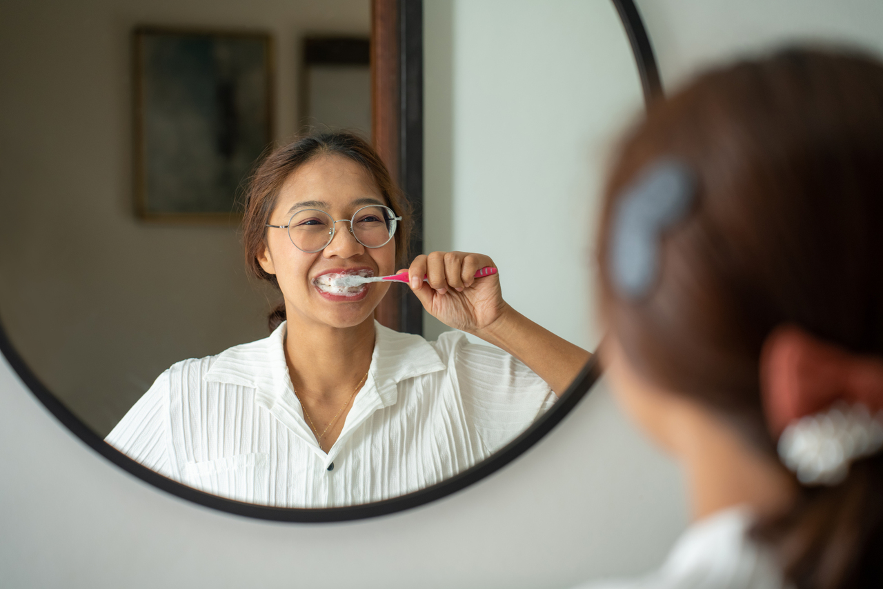 Young lady brushing her teeth in the mirror
