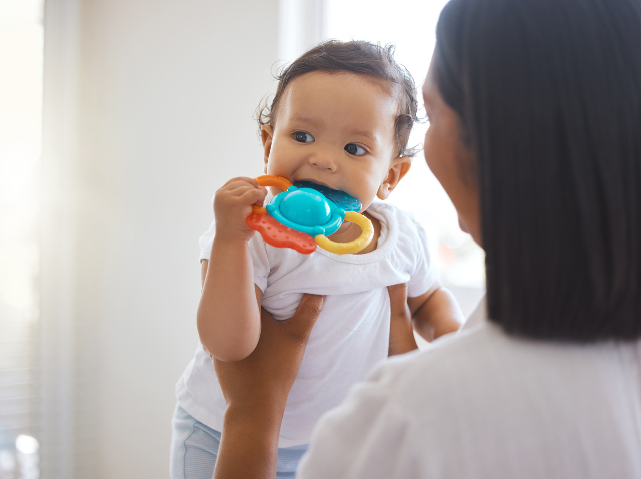 baby playing with teether while being carried by mother