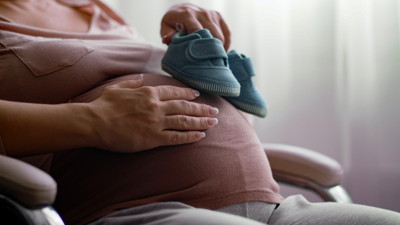 Expectant woman holds blue baby shoes inside home 2026 03 16 05 13 06 utc 1
