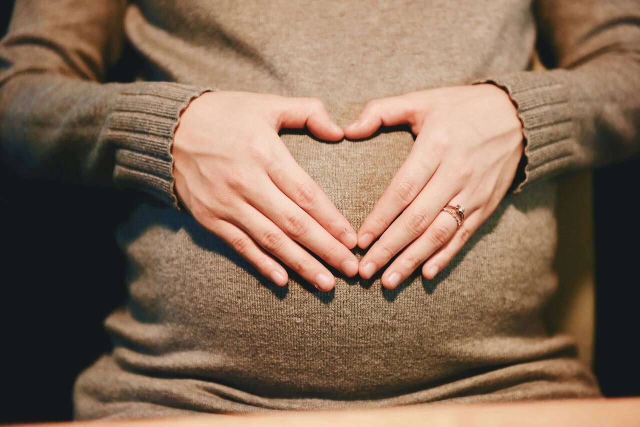 Pregnant woman in gray sweater hands together form heart shape